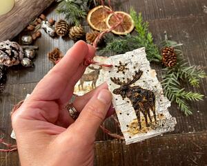 A natural gift tag with a moose wood-burned onto the bark. Tag has a rustic cord tied to a hole in the top corner. 